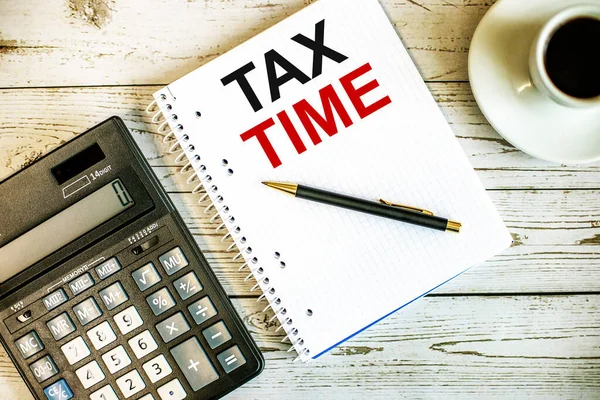 TAX TIME written on white paper near coffee and calculator on a light wooden table. Business concept