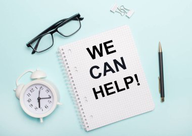 Açık mavi arka planda siyah bir gözlük ve bir kalem, beyaz bir çalar saat, beyaz ataçlar ve yardım edebileceğimiz kelimelerle dolu bir defter var. İş konsepti