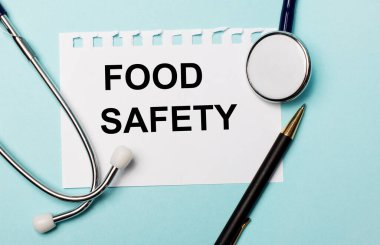 Açık mavi bir arkaplanda, steteskop, bir kalem ve üzerinde Gıda Güvenliği yazan bir kağıt. Tıbbi konsept