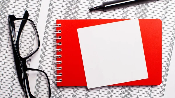 On the desktop are reports, a red notepad, a marker, black-framed glasses and a white sheet of paper for writing. Top view with copy space. Business concept