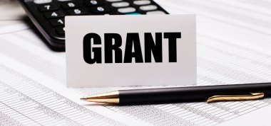 Masanın üzerinde raporlar, bir kalem, bir hesap makinesi ve GRANT yazılı beyaz bir kart var. Odaklanmayın