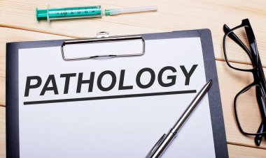 PaTHOLOGY kelimeleri siyah çerçeveli gözlük, kalem ve şırınganın yanındaki beyaz bir kağıt parçasına yazılmıştır. Tıbbi konsept