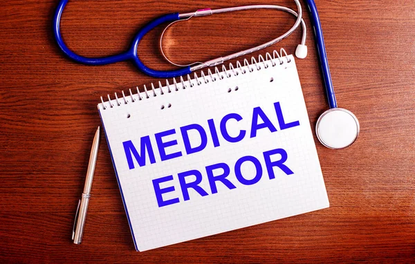 On a wooden table are a pen, a stethoscope, and a notebook labeled MEDICAL ERROR. Medical concept