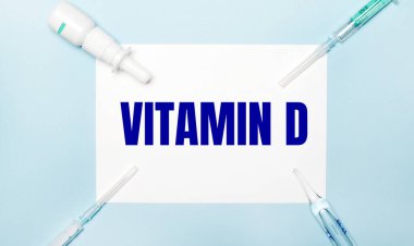 Açık mavi arka planda, şırıngalar, ilaç şişesi, ampul ve üzerinde VITAMIN D. yazan beyaz bir sayfa. Tıbbi konsept..