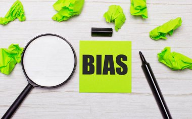 BIAS kelimesi yeşil yapışkan bir nota, büyüteç ve ahşap bir masanın üzerindeki siyah bir kalemle yazılmıştı.
