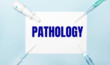 Açık mavi arka planda, şırıngalar, ilaç şişesi, ampul ve PathOLOGY yazılı beyaz bir kağıt. Tıbbi konsept.
