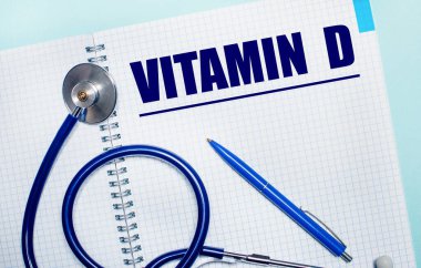 Açık mavi arka planda, üzerinde VITAMIN D, mavi kalem ve stetoskop olan açık bir defter. Yukarıdan bak. Tıbbi konsept