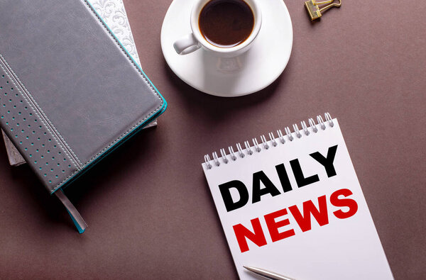 На коричневом фоне, дневники, чашка белого кофе и блокнот с дневными новостями