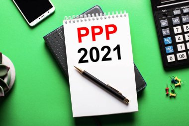 Yeşil arkaplanda - bir telefon, bir hesap makinesi ve PPP 2021 yazıtlı bir günlük