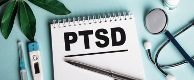 Mavi bir arka planda beyaz bir defterde, deri değiştirici, stetoskop, şırınga ve elektronik termometre yanında, PTSD kelimesi yazılır. Tıbbi konsept