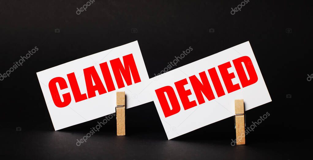 On a black background on wooden clothespins, two white blank cards with the text CLAIM DENIED.