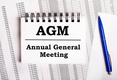 Masada, üzerinde AGM Genel Kurul sözlerinin yer aldığı mavi bir kalem ve bir defter bulunan tablolar ve raporlar bulunuyor.