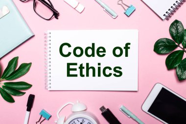 ETHICS 'in kodu, iş aksesuarları ve yeşil yapraklarla çevrili pembe bir arka plan üzerine beyaz bir deftere yazılmıştır..