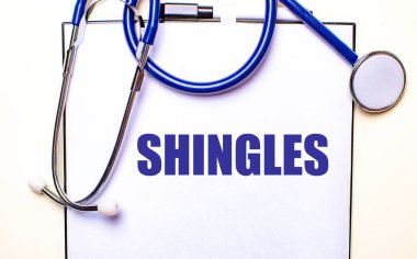 SHINGLES kelimesi steteskopun yanındaki beyaz bir çarşafa yazılmıştır. Tıbbi konsept