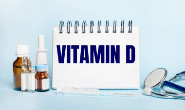 Hafif bir arka planda, bir şırınga, bir stetoskop, ilaç şişeleri, bir ampul ve VITAMIN D yazılı beyaz bir not defteri.