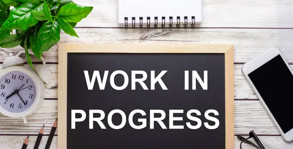 PROGRESS 'te Çalışma Kalemlerin yakınındaki siyah bir arkaplanda, bir akıllı telefon, beyaz bir not defteri ve tencerede yeşil bir bitki