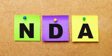 Bej bir arka planda, NDA Non Revclosure Agreements sözcüğüyle notlar için çok renkli çıkartmalar