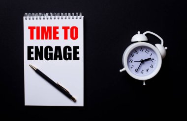 Bağlanma zamanı siyah zemin üzerinde beyaz bir çalar saatin yanında beyaz bir not defterine yazılır..