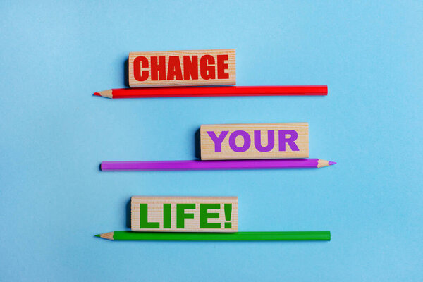 На синем фоне, три цветных карандаша, три деревянных блока с текстом Изменить свою жизнь