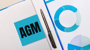 Üzerinde AGM Yıllık Genel Kurul metni olan mavi yapışkan notla mavi çizelge arasında bir kalem var. İş konsepti. Yukarıdan görüntüle