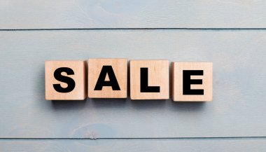 Açık mavi ahşap arka planda satılan metni olan tahta küpler..