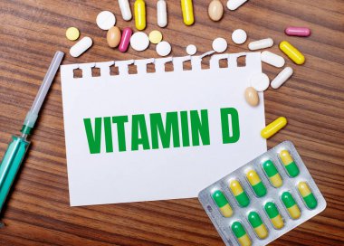 Tahta bir masaya, şırıngaya, haplara ve üzerinde VITAMIN D yazılı bir kağıt parçasına.