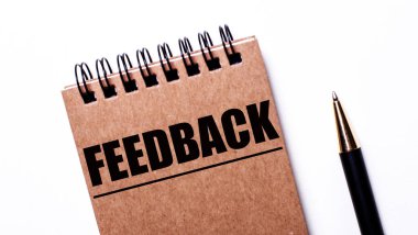 Hafif arkaplanda siyah bir kalem ve siyah yaylı kahverengi bir defter var. Üzerinde FEEDback yazıyor.