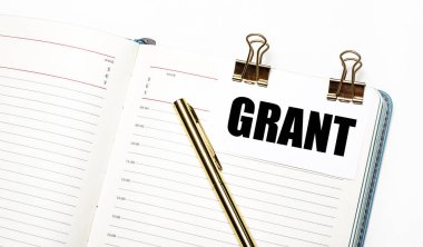 Hafif bir arka planda, açık bir defter, altın ataçlı bir kağıt, GRANT metni ve altın bir kalem. Yukarıdan bak. İş konsepti