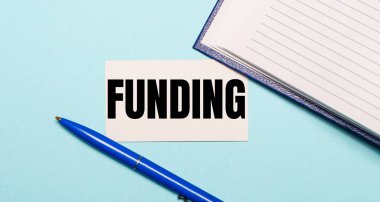 Not defteri, beyaz kalem ve kart. Üzerinde mavi arka planda yazılar var. Yukarıdan görüntüle