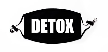 Açık arkaplanda siyah tıbbi yüz maskesi ve üzerinde DETOX yazıyor. Hastalık önleme. Tıbbi konsept