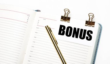 Hafif bir arka planda, açık bir defter, altın ataçlı bir kağıt ve BONUS metni ve altın bir kalem. Yukarıdan bak. İş konsepti