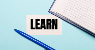 Notepad, white pen and card with the inscription LEARN on a blue background. View from above