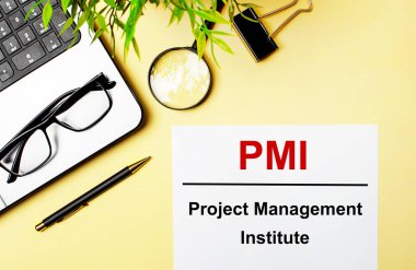 PMI Proje Yönetimi Enstitüsü, dizüstü bilgisayar, kalem, büyüteç, gözlük ve yeşil bitkinin yanında açık sarı zemin üzerinde beyaz bir kağıt parçasına kırmızı ile yazılmıştır..