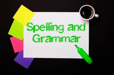 Üzerinde Heceleme ve Gramer yazan bir kağıt, bir fincan kahve, notlar için parlak renkli çıkartmalar ve siyah arka planda yeşil bir kalem. Yukarıdan görüntüle.