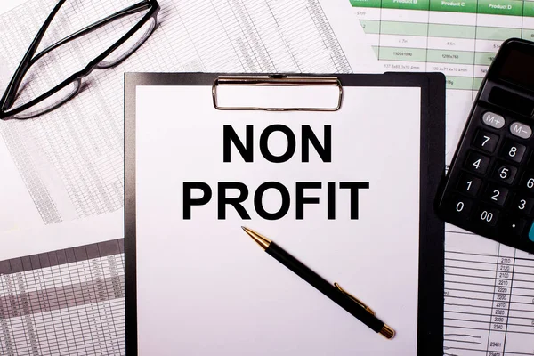 NON PROFIT is written on a white sheet of paper, near the glasses and the calculator.