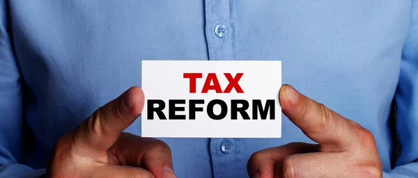 The words TAX REFORM is written on a white business card in a man\'s hands. Business concept