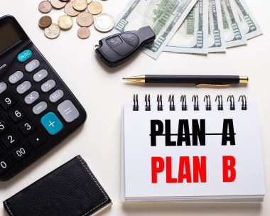 Beyaz bir masada hesap makinesi, araba anahtarı, nakit para, bir kalem ve B yazılı bir defter var.