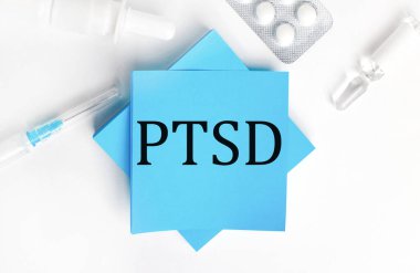 Beyaz arka planda, bir şırınga, ampul, haplar, bir şişe ilaç ve üzerinde travma sonrası stres bozukluğu yazan açık mavi çıkartmalar. Tıbbi konsept