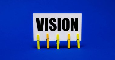 Sarı mandallar üzerinde parlak mavi bir zemin üzerinde VISION yazılı beyaz bir kart