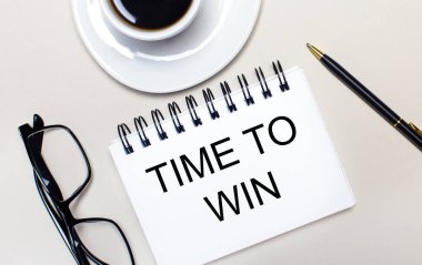Gözlük, beyaz bir fincan kahve, Time to WIN yazan beyaz bir defter ve arka planda tükenmez kalem. Düz yatıyordu. Yukarıdan görüntüle.