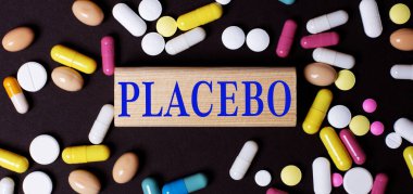 Karanlık bir arka planda, çok renkli haplar ve tahta bir blokta PLACEBO kelimesi. Tıbbi konsept