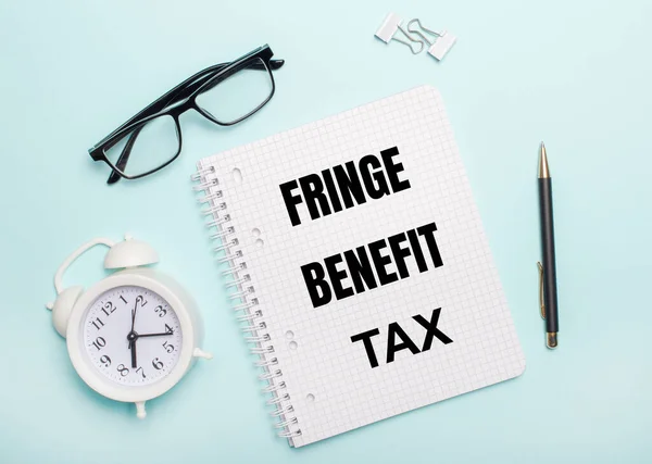 Açık mavi bir arka planda siyah gözlük ve bir kalem, beyaz bir çalar saat, beyaz ataçlar ve FRINGE BENEFIT Vergi yazılı bir defter bulunur. İş konsepti