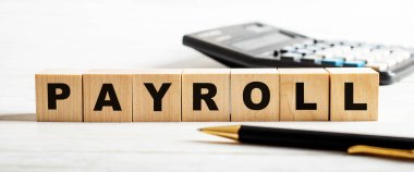 PAYROLL kelimesi bir hesap makinesi ve bir kalem arasındaki tahta küplere yazılmıştır. İş konsepti. Odaklanmayın