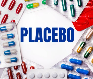 PLACEBO kelimesi, içinde haplar olan çok renkli paketlerle çevrili açık bir arkaplana yazılmıştır. Tıbbi konsept