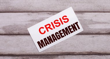 Ahşap bir arka planda kırmızı metin CRISIS MANAGEMENT yazılı beyaz bir kart var.