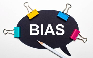 Açık arkaplanda, çok renkli ataçlar, üzerinde BIAS yazan beyaz bir kalem ve siyah kağıt var. Yukarıdan görüntüle