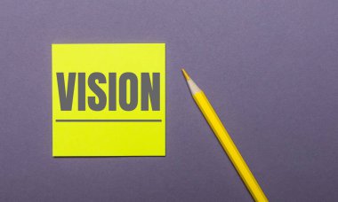 Gri bir arka planda, parlak sarı bir kalem ve üzerinde VISION yazan sarı bir çıkartma.