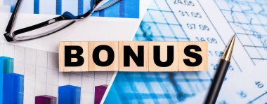 Parlak diyagramlarda, gözlüklerde, bir kalem ve tahtadan küplerde BONUS yazıyor. İş konsepti