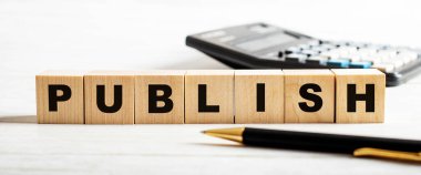 Hafif arkaplanda, bir kalem, hesap makinesi ve üzerinde PUBLISH yazan tahta küpler. Odaklanmayın