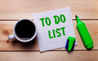 Tahta bir masa, bir fincan kahve, yeşil bir kalem ve yapılacaklar listesi yazılı bir peçete.